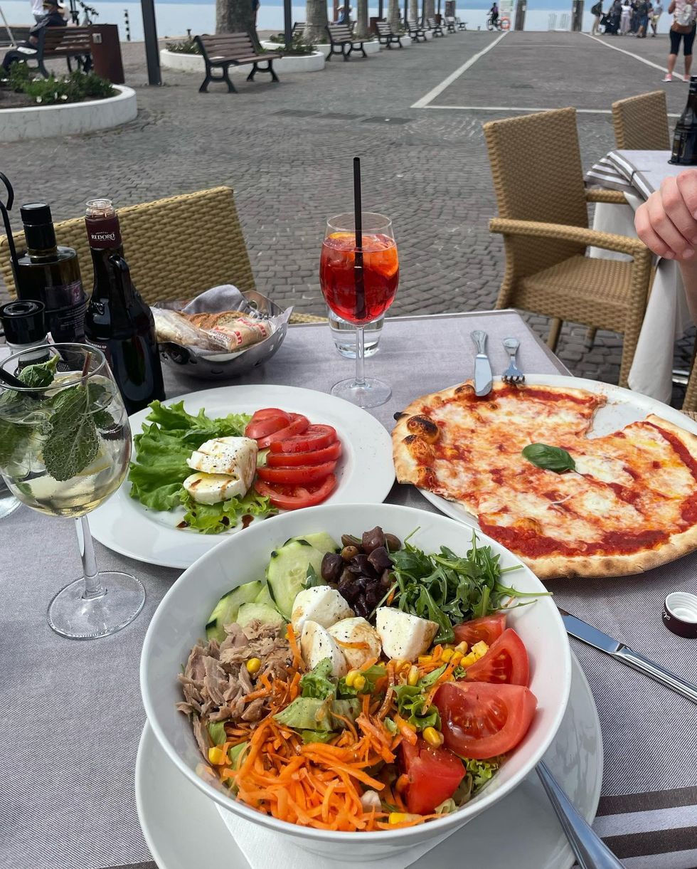 A table in Torri Del Benaco full of salad, pizza, and caprese with spritz cocktails.
